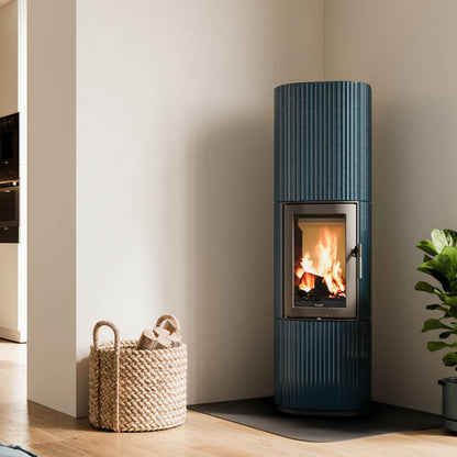 LEDA SANNA Speicherofen in Petrolblau mit emaillierter Gussoberfläche, geriffeltem Design und großzügiger Feuersicht.